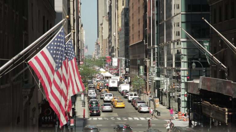 two american flags are flying in a busy street.