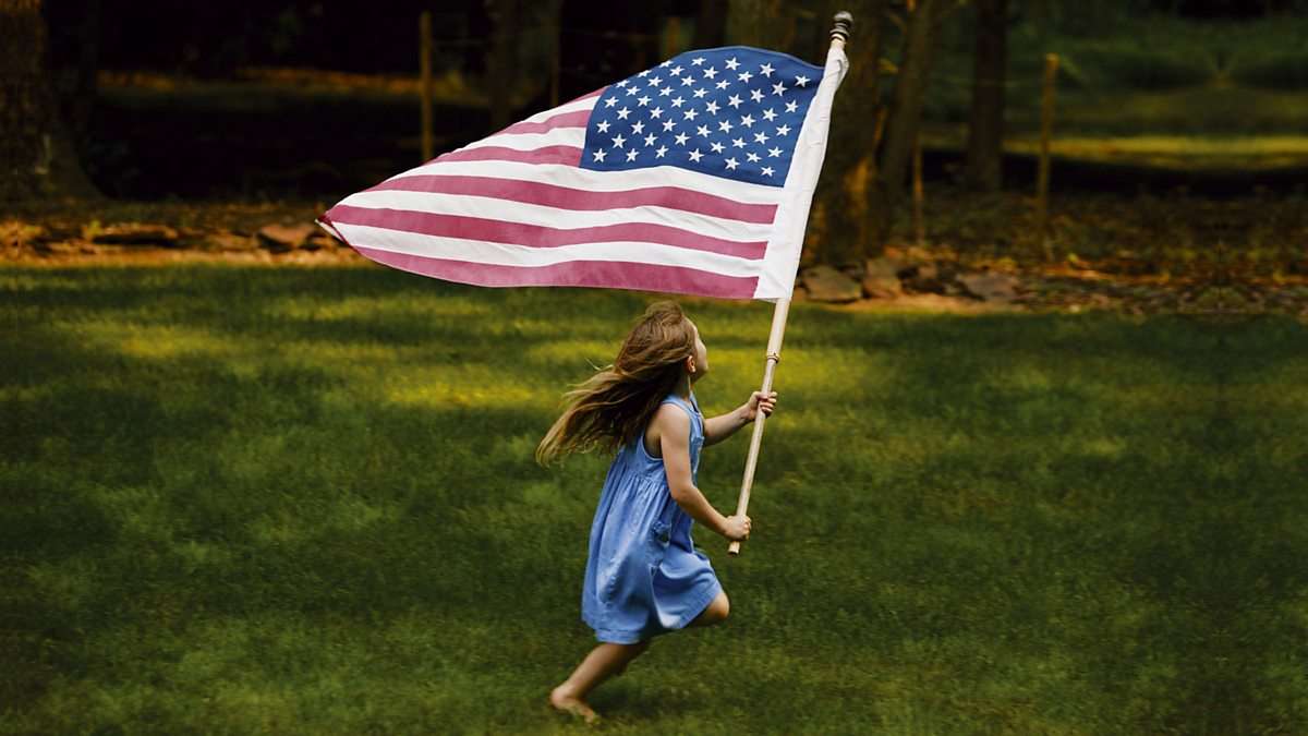 a little girl is running holding an American flag.
