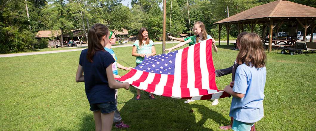 kids in a ground holding a flag, they are folding the American flag.