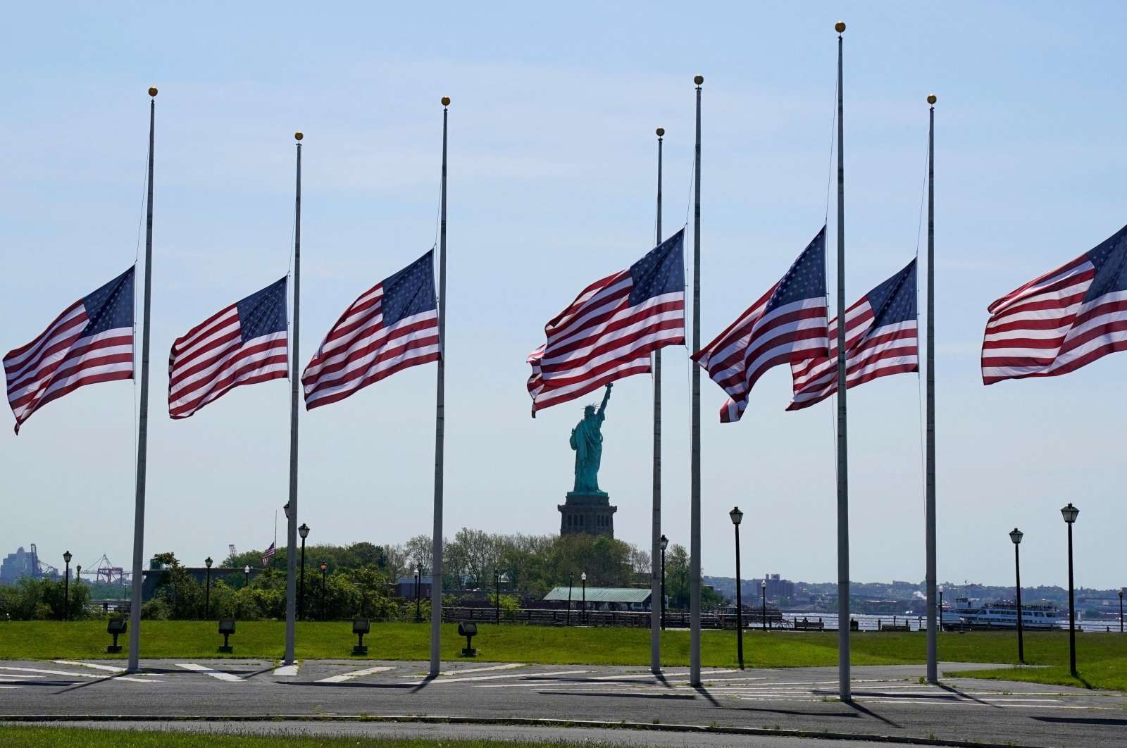 American flags flying at half mast in front of statue of liberty.