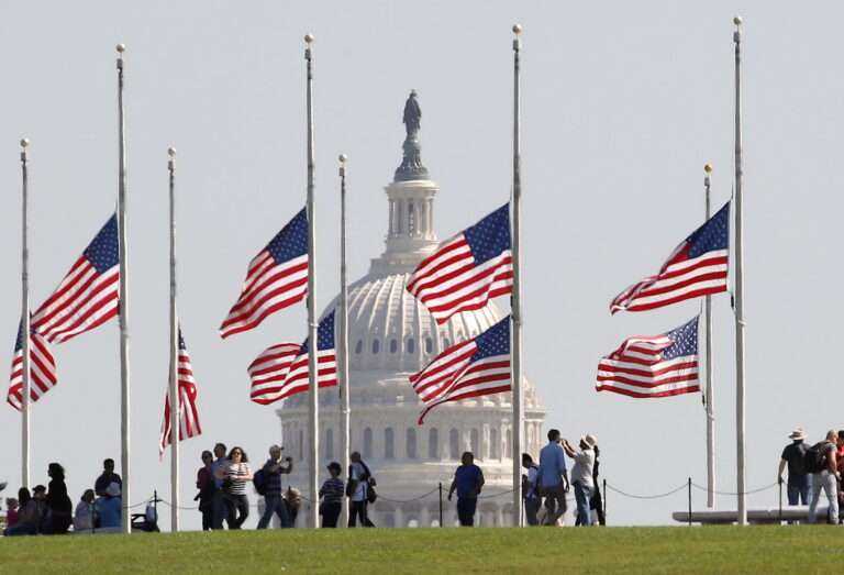 American flags flying at half mast in front state building.