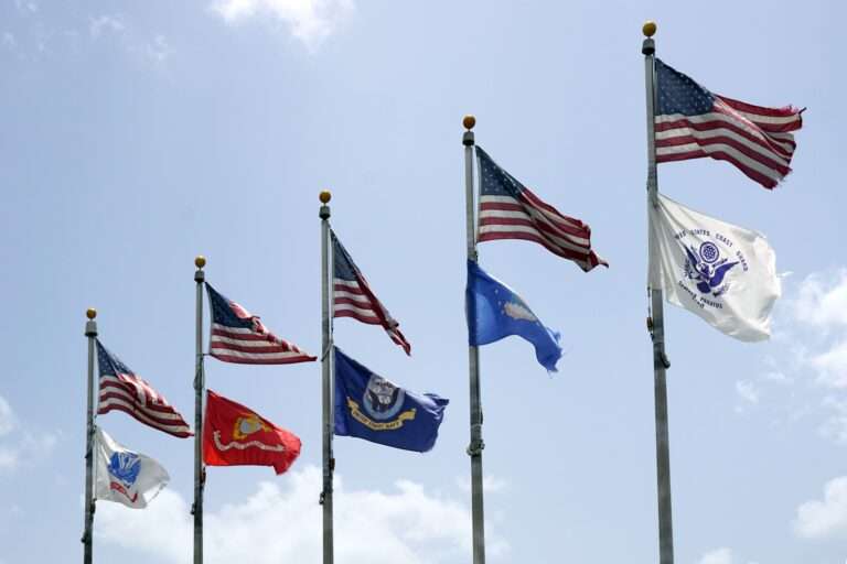 5 different army flags flying under the American flag on polls.