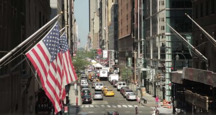 two american flags are flying in a busy street.