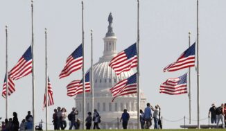 American flags flying at half mast in front state building.