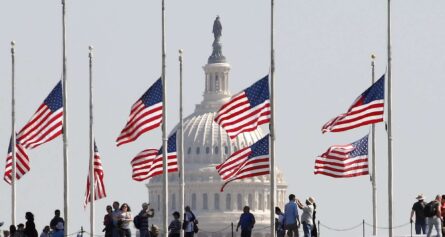 American flags flying at half mast in front state building.