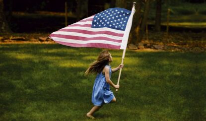 a little girl is running holding an American flag.