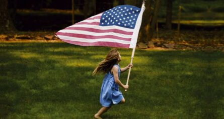 a little girl is running holding an American flag.