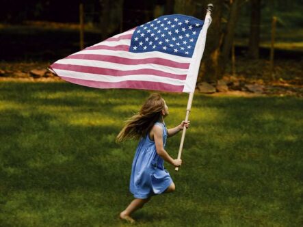 a little girl is running holding an American flag.