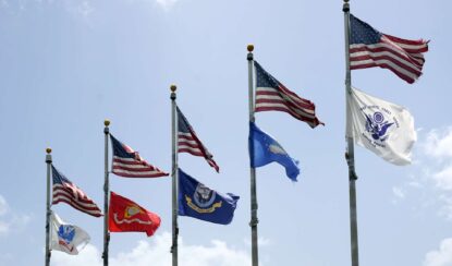 5 different army flags flying under the American flag on polls.